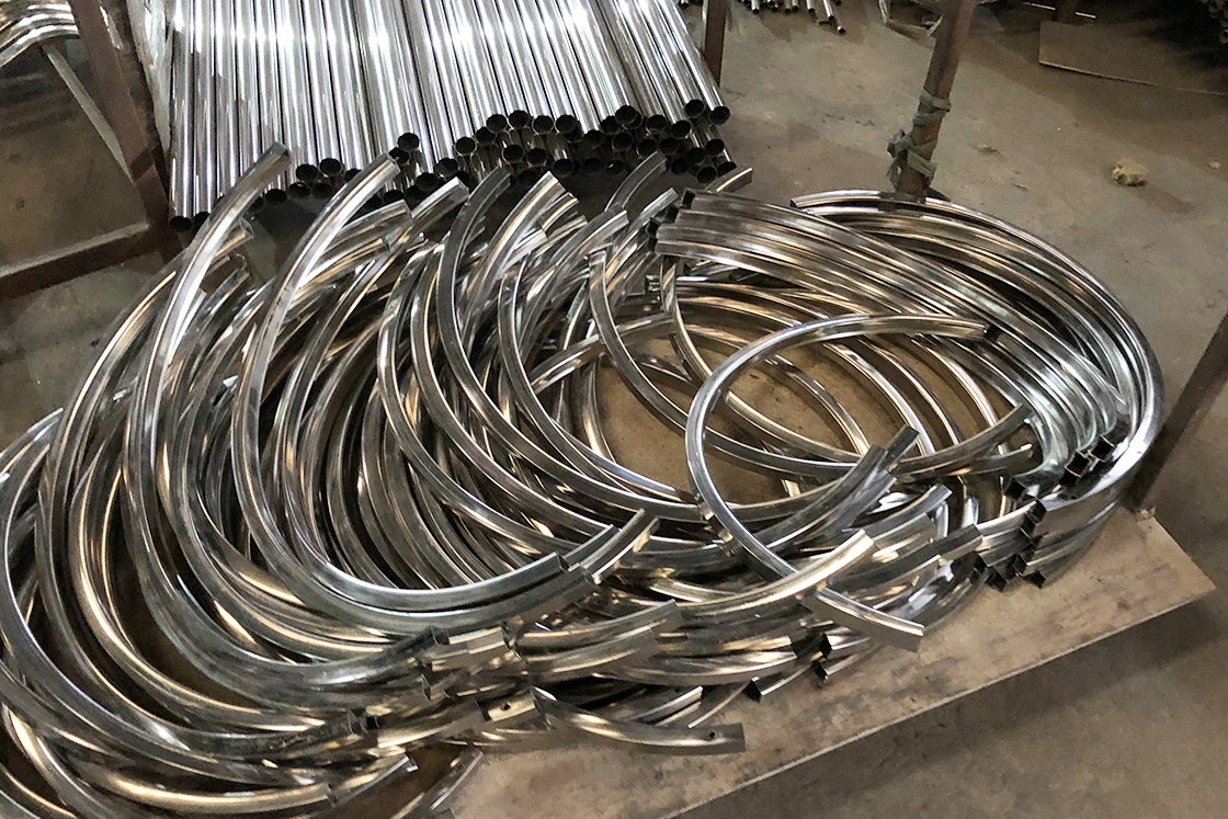 Stack of curved stainless steel tubes for metal chair frames in factory.