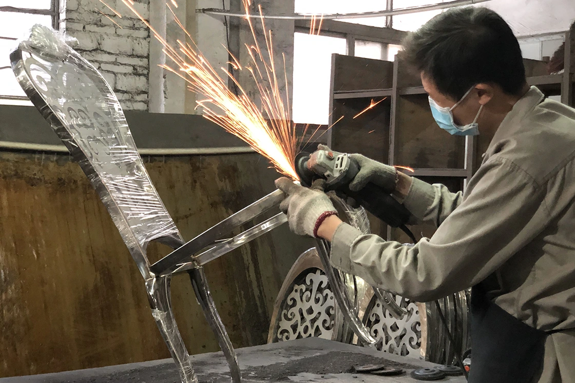 Factory worker grinding and smoothing a stainless steel chair frame with sparks flying.
