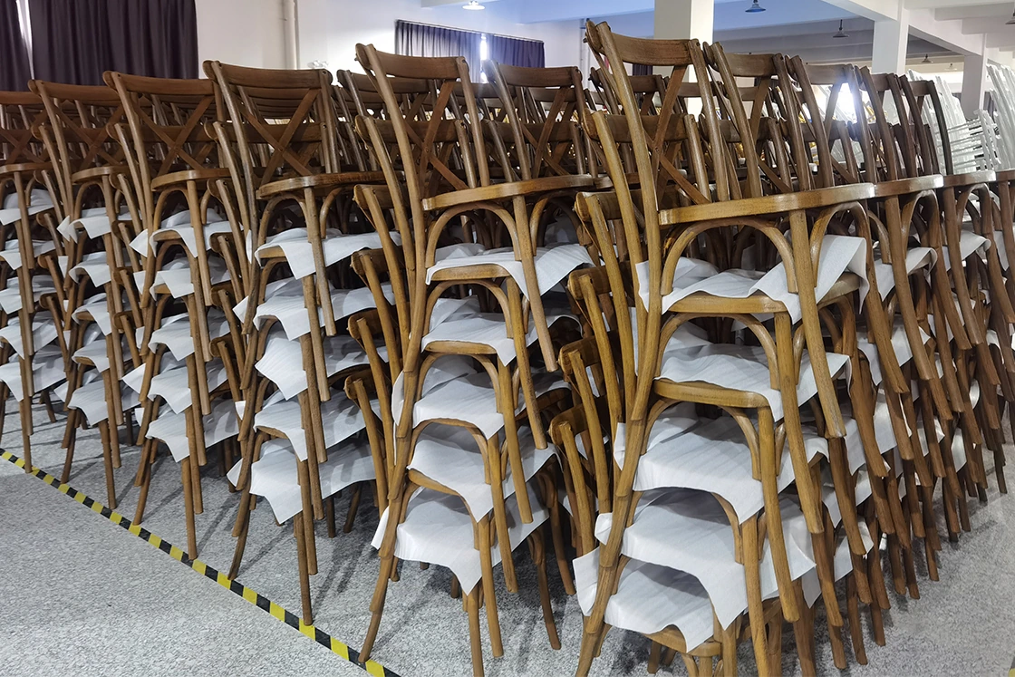 Large inventory of wooden cross-back event chairs stacked in warehouse.