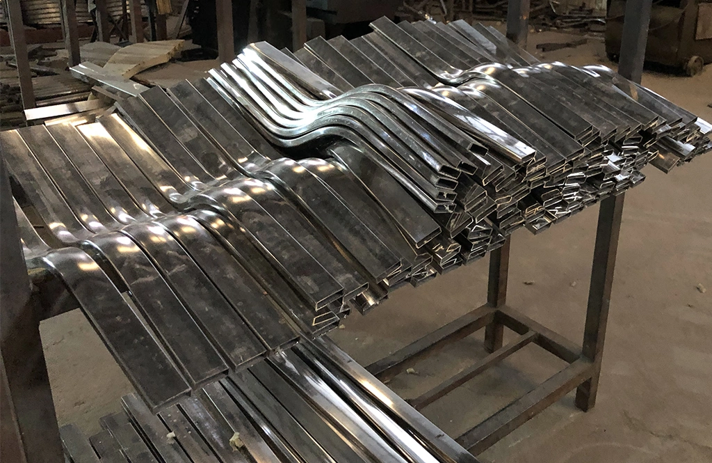 Stacks of curved stainless steel rectangular tubes ready for furniture assembly.