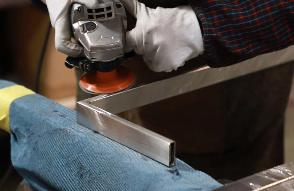 Worker using an angle grinder to smooth the edges of a metal furniture component.