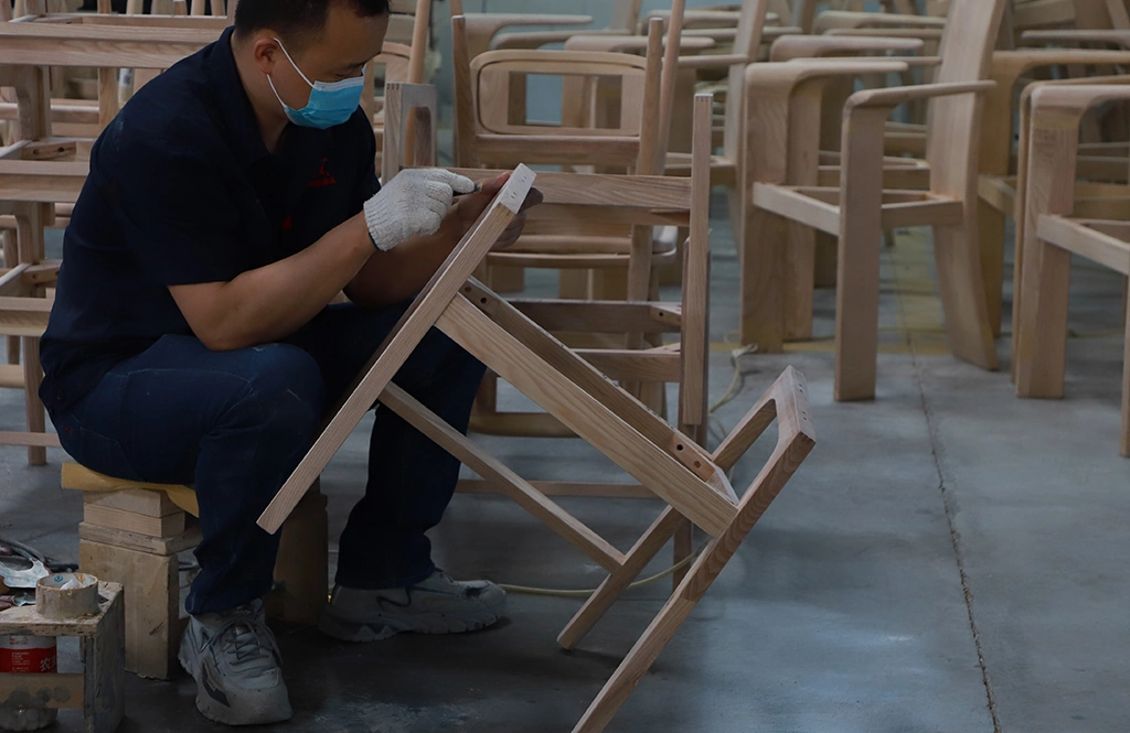 Craftsman sanding and assembling the joints of a solid wood chair frame.