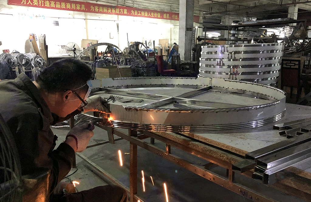 Professional welder working on a large circular stainless steel frame with sparks flying.
