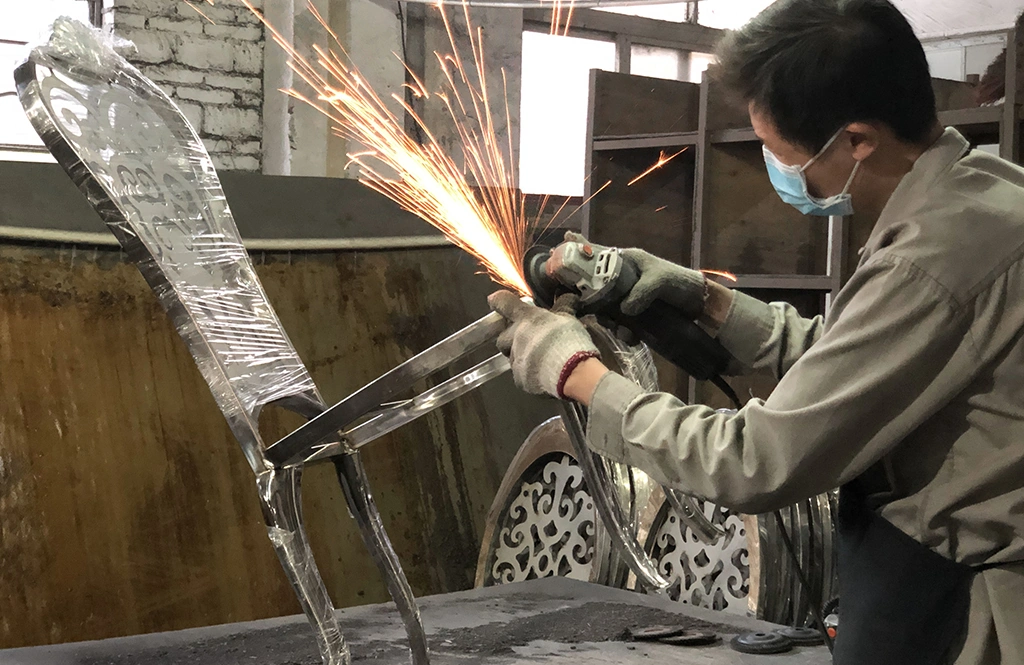 Worker polishing a Louis chair stainless steel frame to a mirror-like finish.