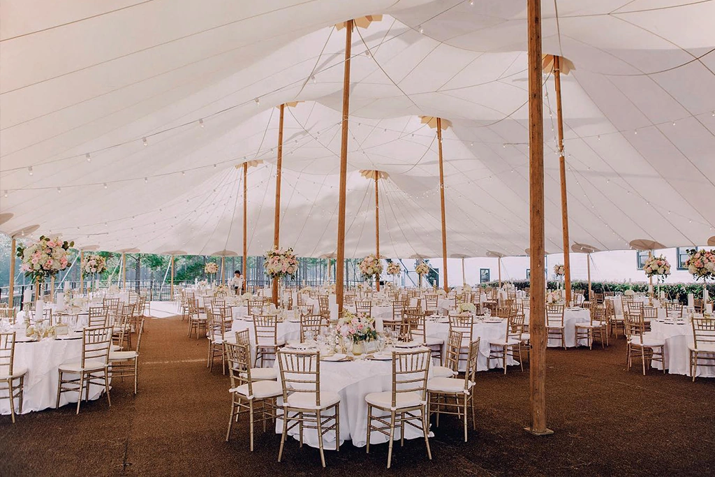 Gold Chiavari chairs filling a large white marquee tent with high peaks.