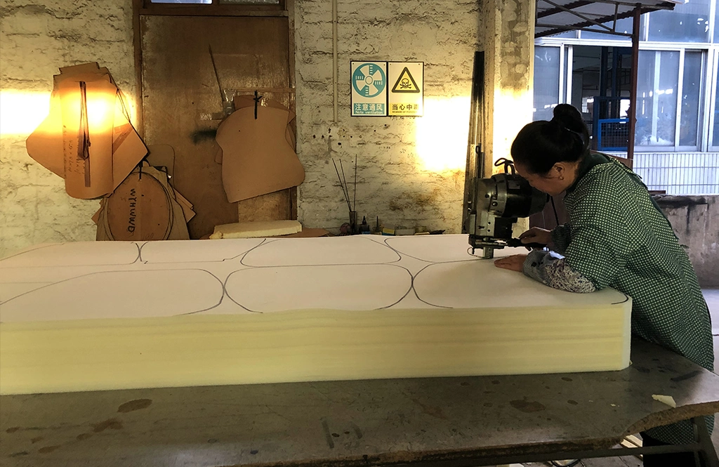 Worker using a vertical fabric cutter to slice through a thick layer of high-density foam.