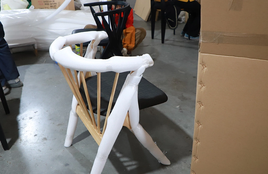 Wrapping a finished wooden chair with protective foam after quality inspection.