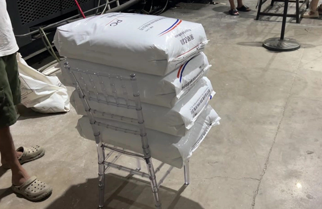 Heavy bags of raw PC material stacked on a clear resin chair for a load test.