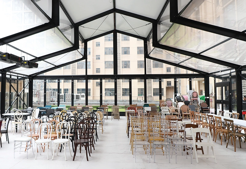 Large glass tent showroom filled with rows of Chiavari, cross-back, and bentwood event chairs.