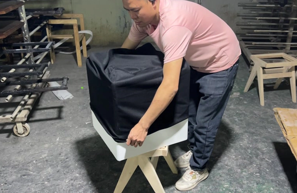Worker fitting a black protective cover over a white furniture cube.