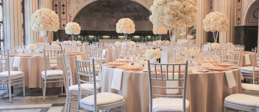 Classic ballroom wedding reception with silver Chiavari chairs, blush tablecloths and tall white floral centerpieces.