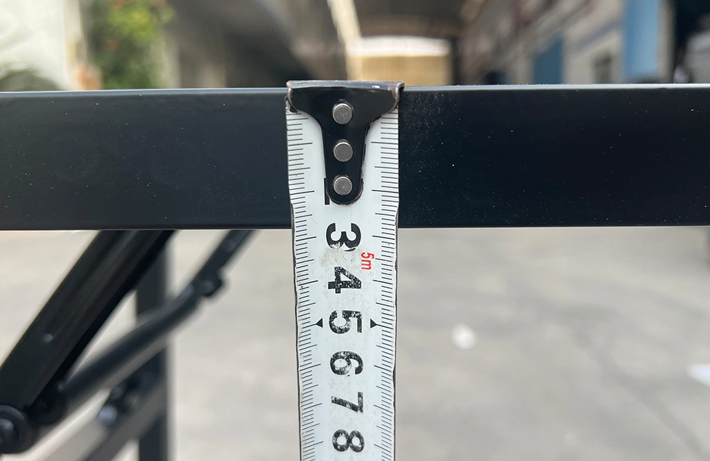 Measuring the profile width of a black metal furniture frame with a tape measure.