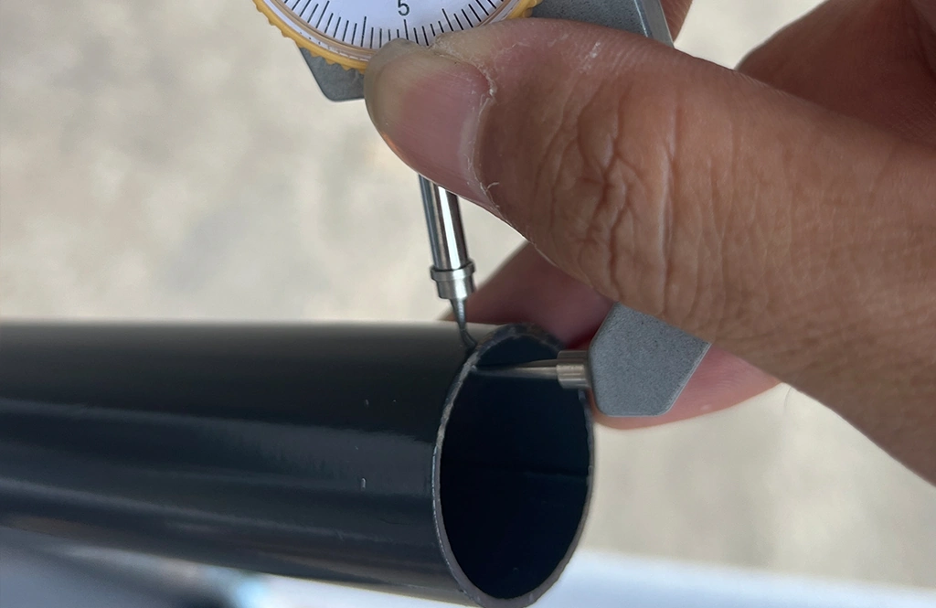 Caliper measuring the wall thickness of a black metal chair tube.